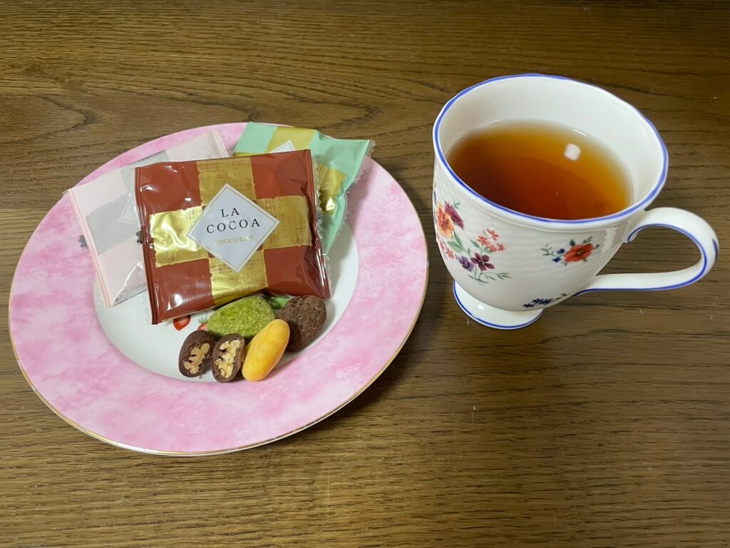 紅茶と一緒に盛り付けられたサロンドロワイヤルのピーカンナッツチョコレート3種。ピンクのティーカップと皿で丁寧におやつタイムを楽しむ様子。