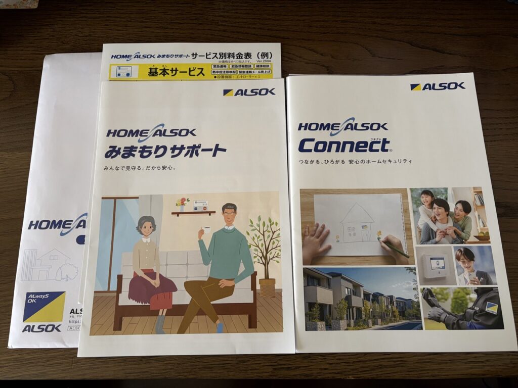 アルソックから届いた資料の写真。みまもりサポートの冊子、HOME ALSOK Connectの冊子、サービス別料金表